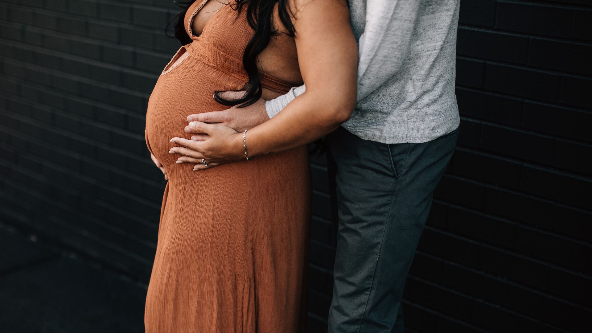 a man standing behind his partner while both rest their hands on her pregnant belly