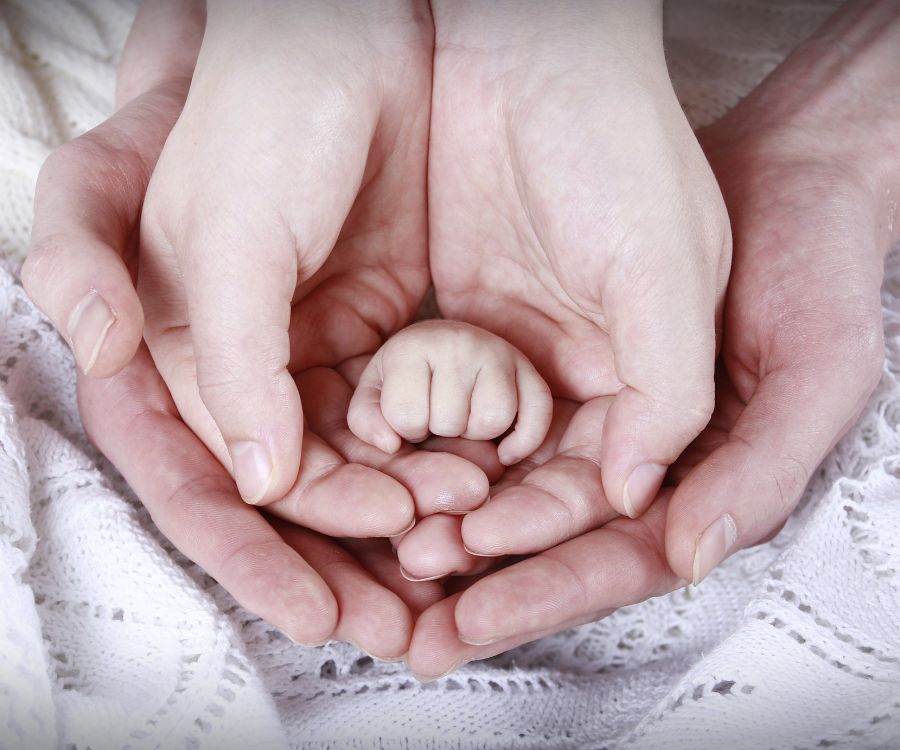 two sets of parents hands with a baby's hand nestled within